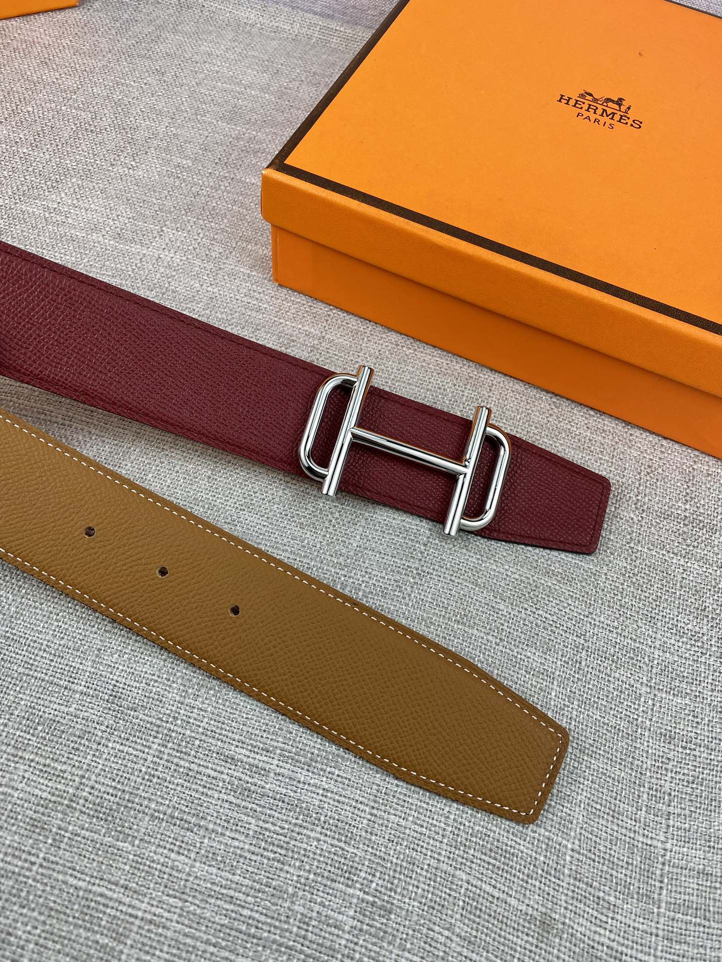 Burgundy leather belt with metallic rectangular buckle and visible strap hole row
