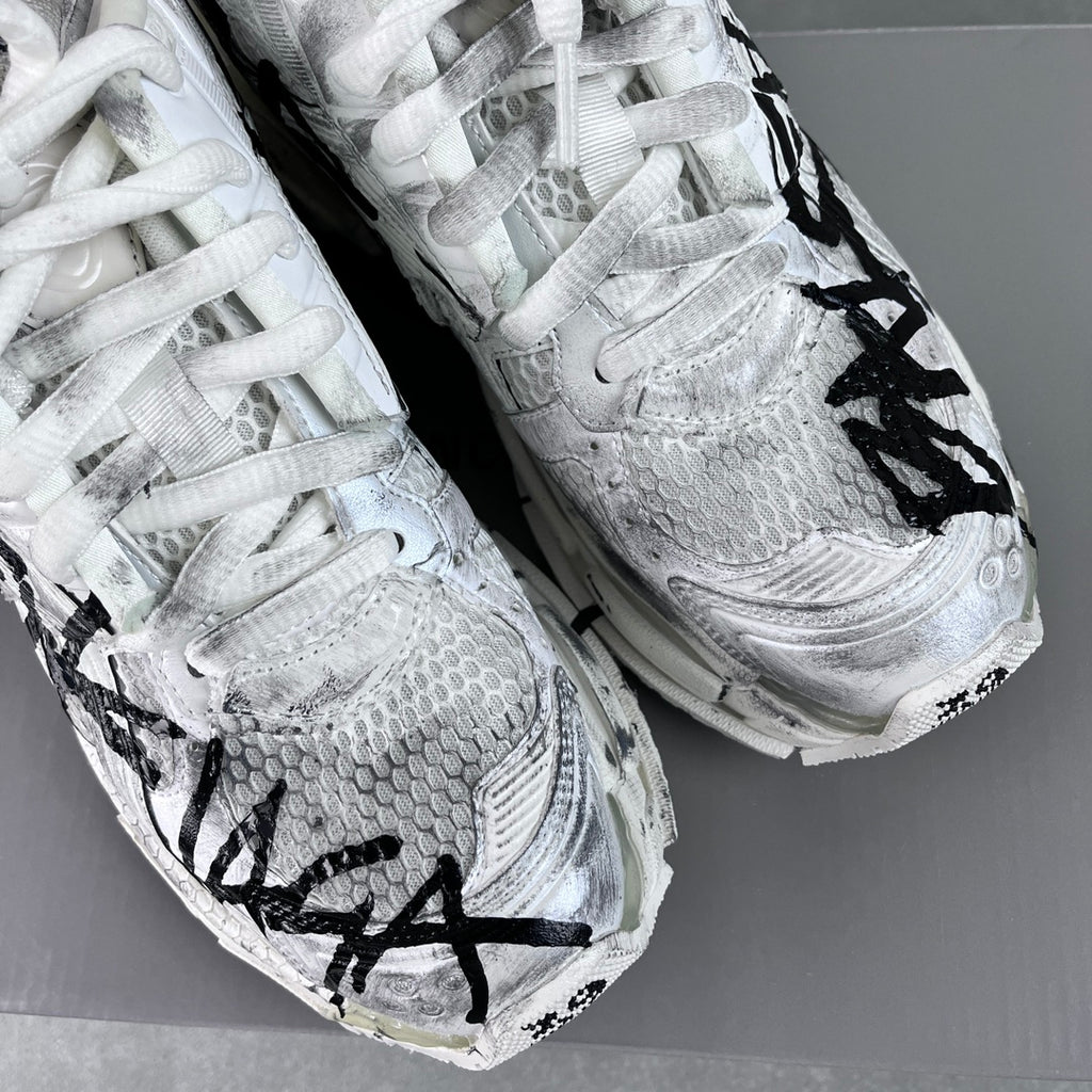 Unisex white sneaker with black graffiti-style print, textured upper, lace-up