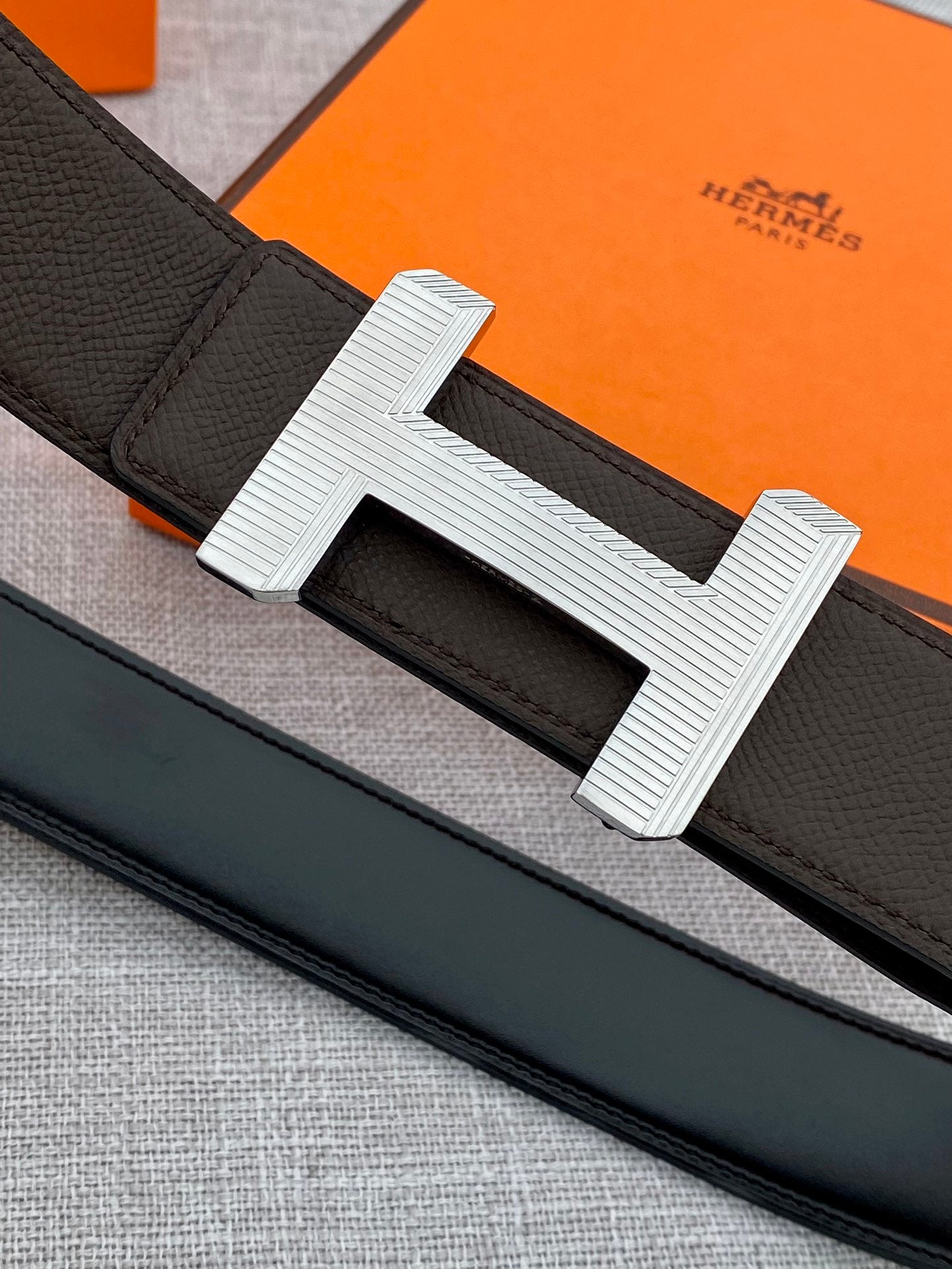 Hermes belt close-up: dark strap with engraved silver-tone H buckle