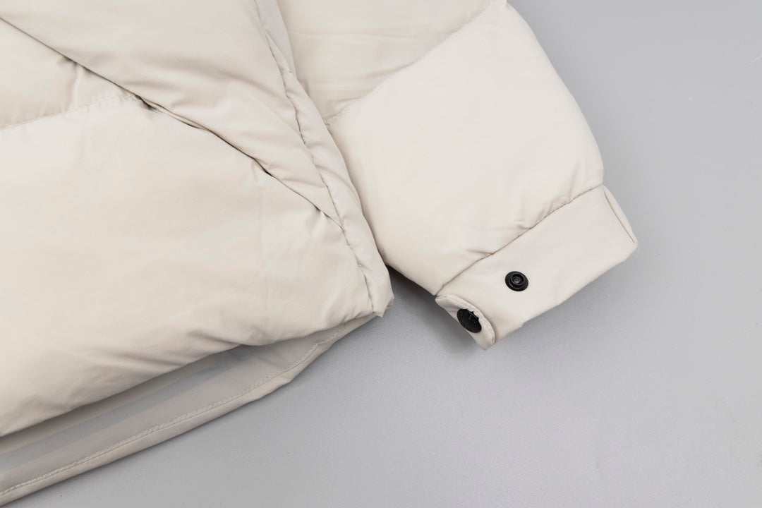 Cream puffer jacket sleeve cuff with black snap buttons and quilted quilting.