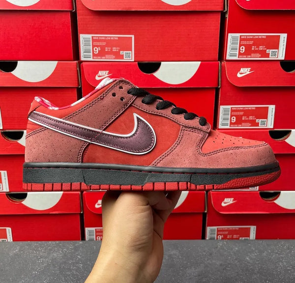 Coral red suede low-top sneaker held up front, black laces and red tread sole