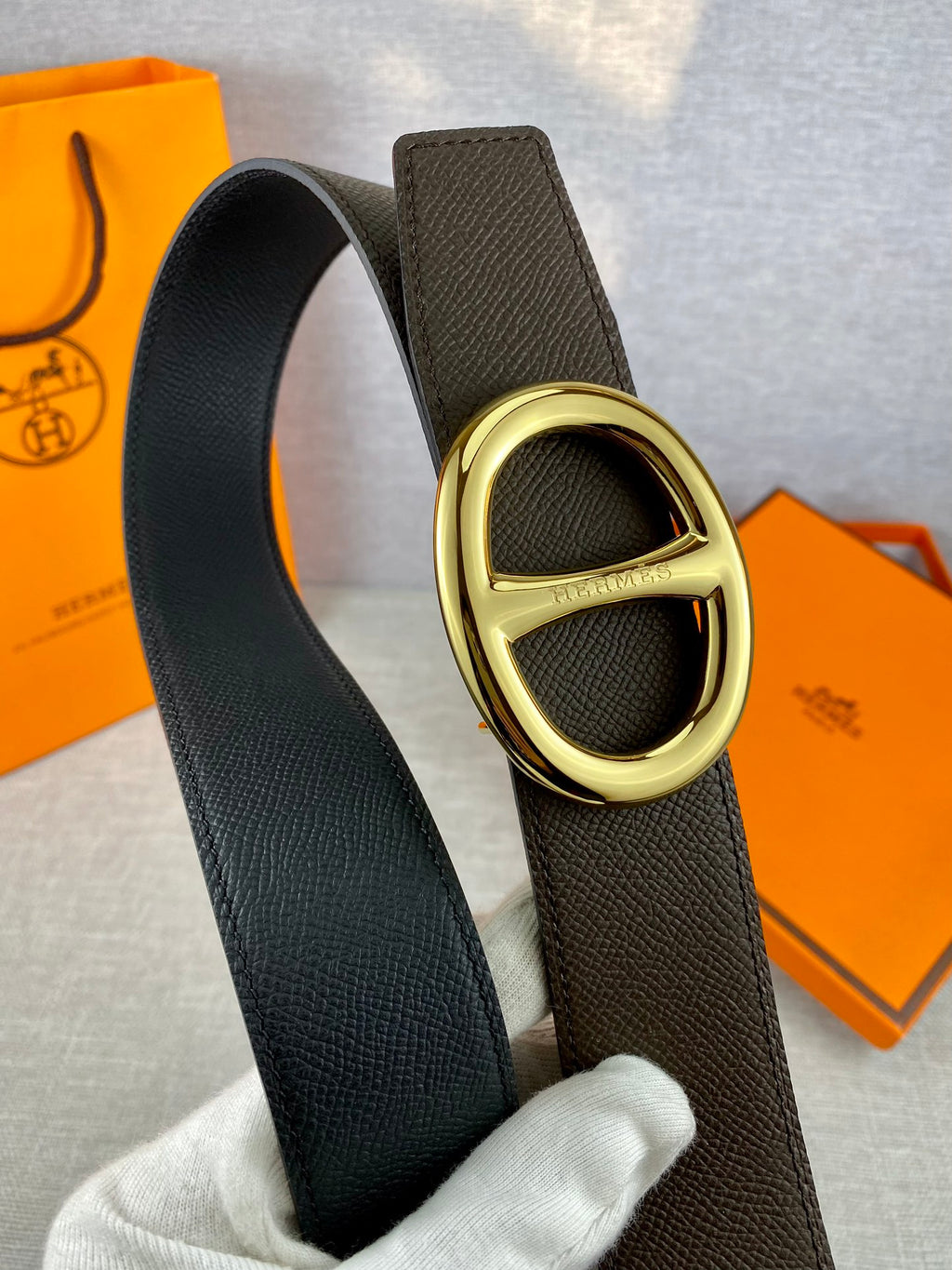 Dark leather belt with gold-tone double H buckle, close-up.