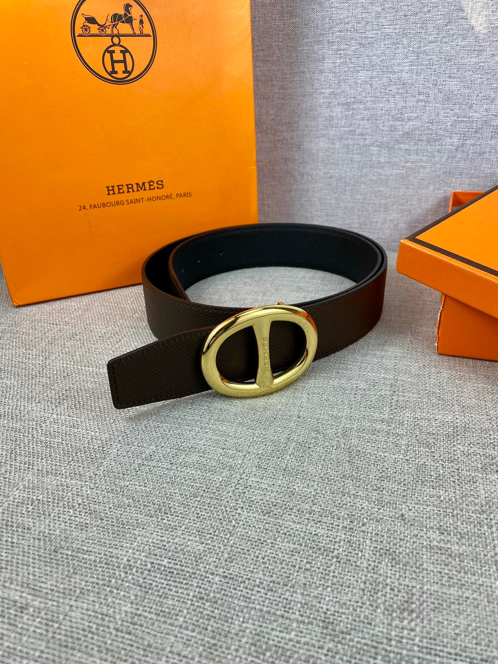 Dark leather belt with gold-tone double H buckle, laid flat.