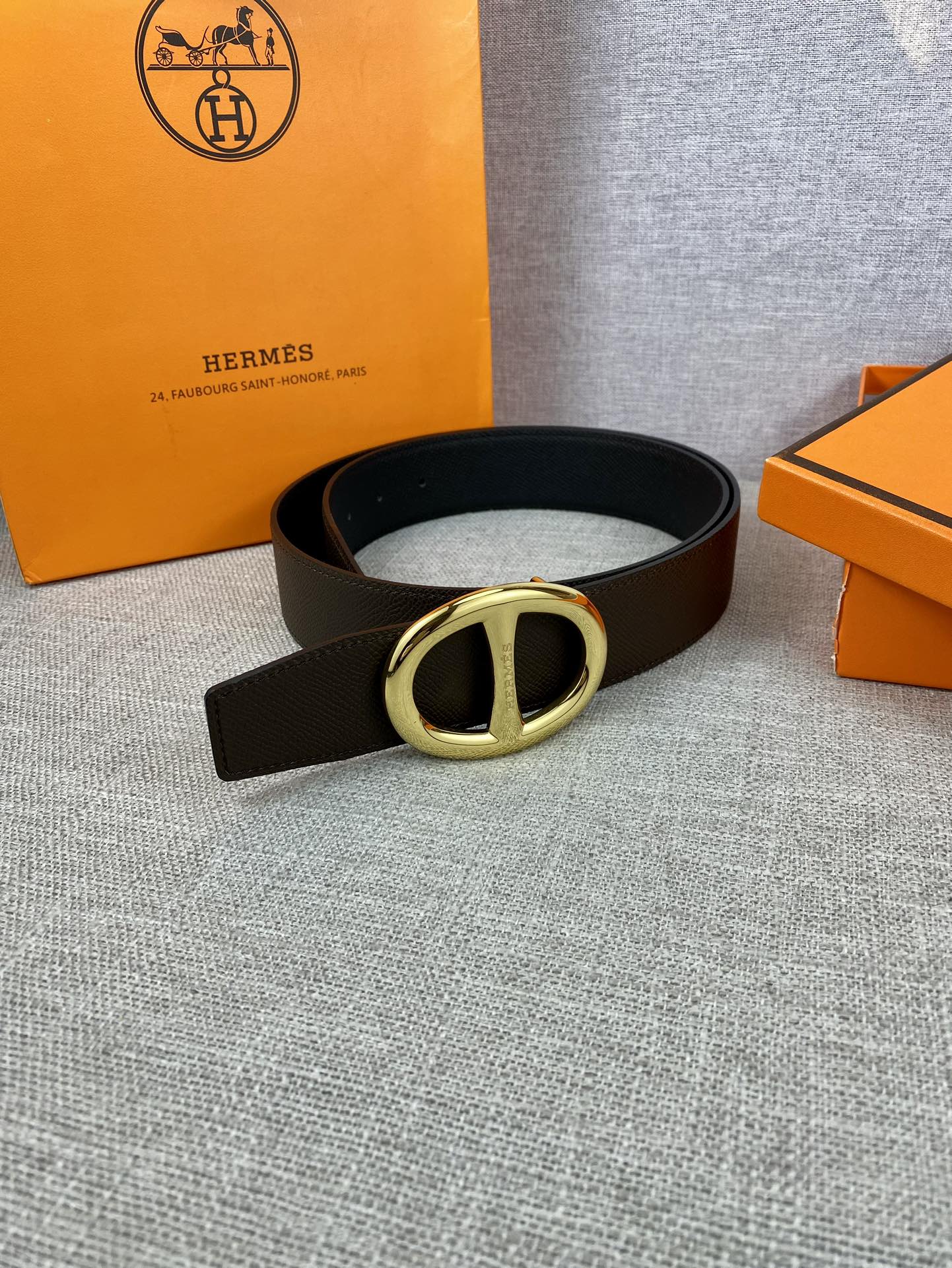 Dark leather belt with gold-tone double H buckle, laid flat.
