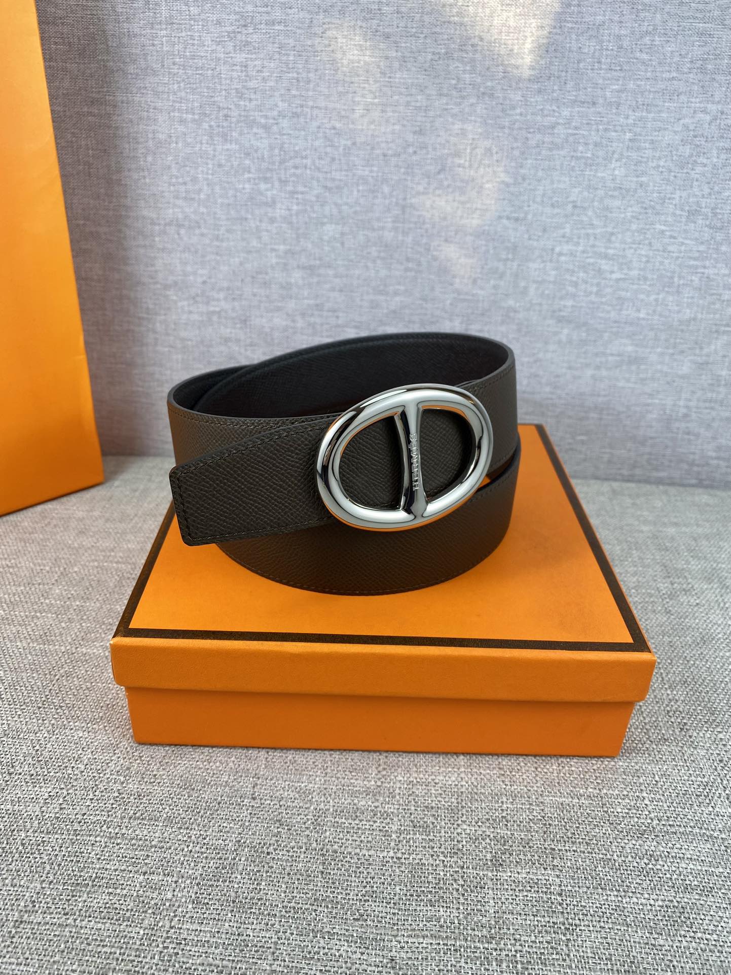 Dark leather belt with silver-tone double H buckle, laid on surface.
