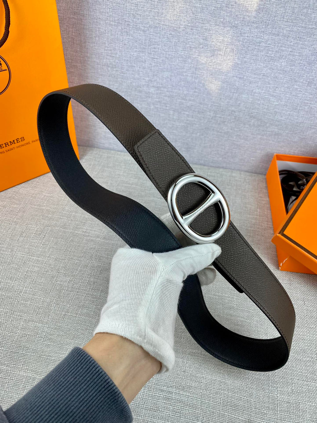Dark leather belt with silver-tone double H buckle, held in hand.