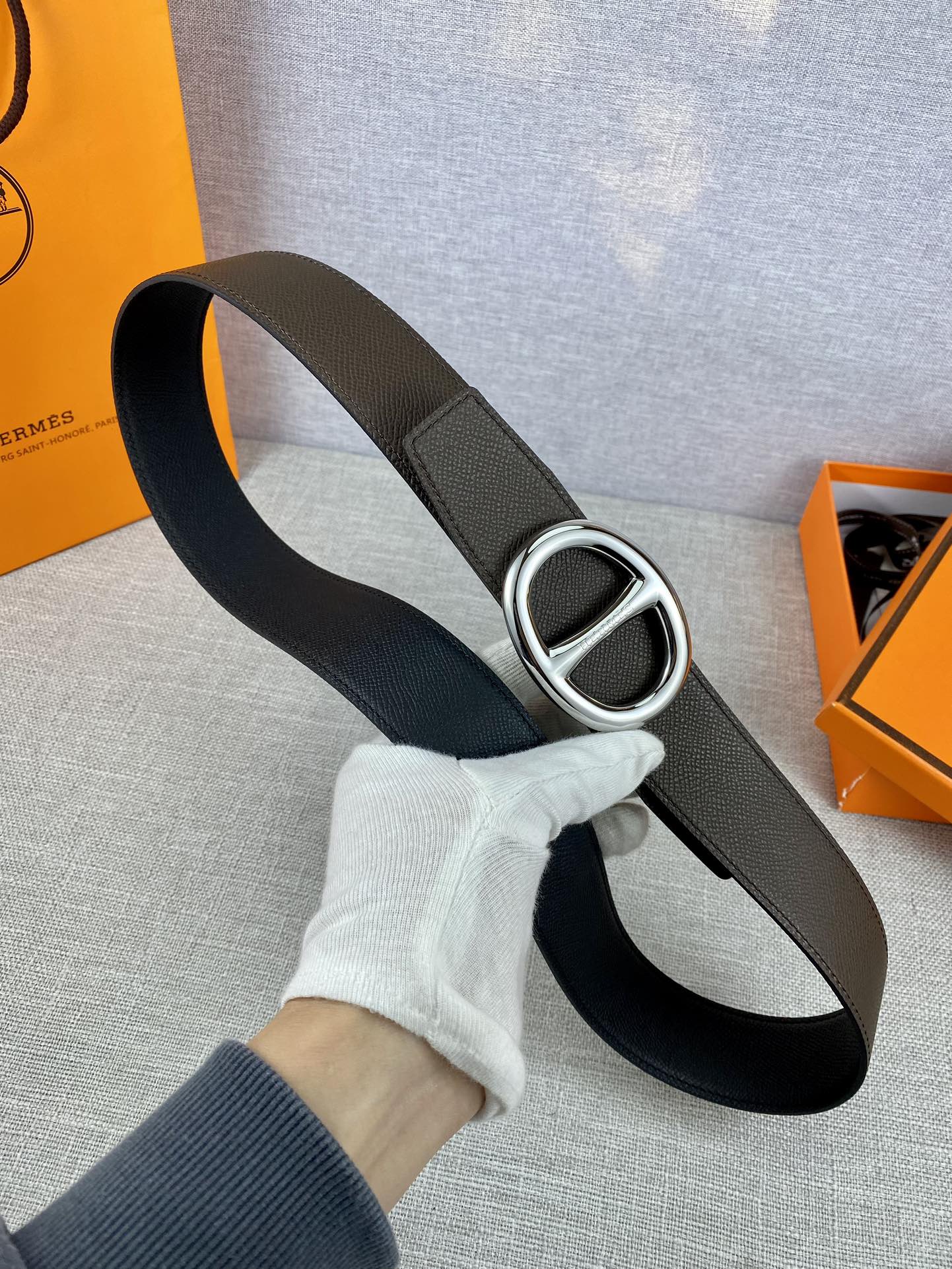Dark leather belt with silver-tone double H buckle, held in hand.