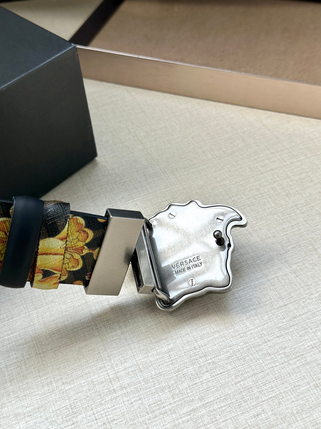 Versace belt close-up: dark blue leather end and baroque strap with Medusa buckle.