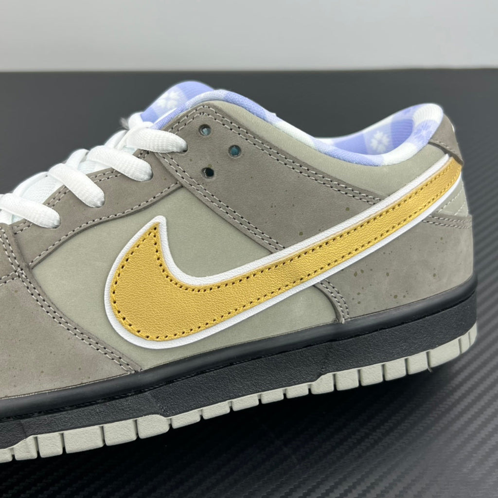 Grey suede sneaker close-up with yellow swoosh, white laces, and black outsole