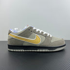 Grey suede low-top sneaker side view with yellow swoosh and white lace-up