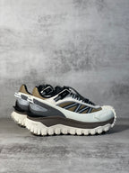 Moncler trail sneaker, angled view, white upper with navy stripe and black accents