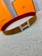 Leather belt with tan strap, gold H buckle, and burgundy inner band on display.