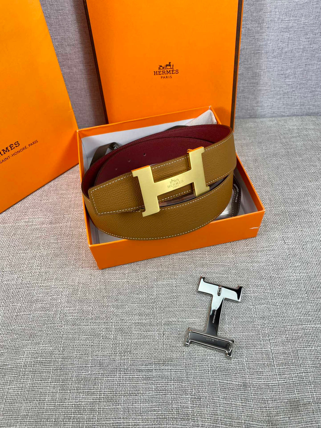 Leather belt in tan and burgundy with gold H buckle, shown in gift box.