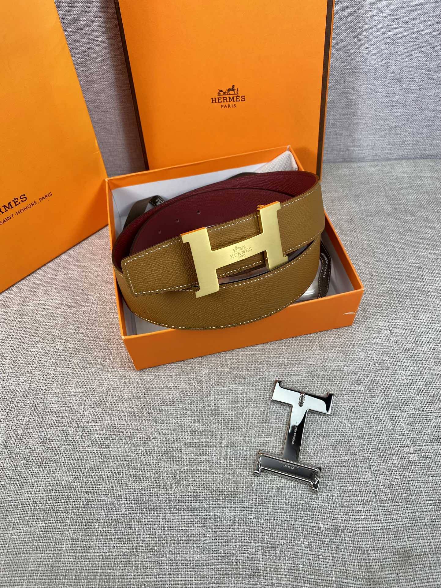 Leather belt in tan and burgundy with gold H buckle, shown in gift box.