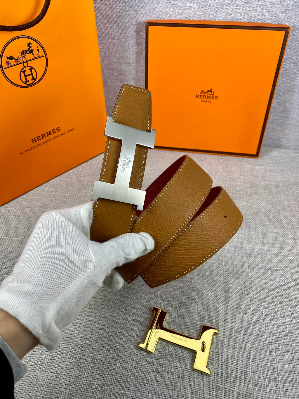Leather belt with tan strap and gold H buckle, burgundy keeper card visible.