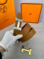 Leather belt with tan strap and gold H buckle, burgundy keeper card visible.