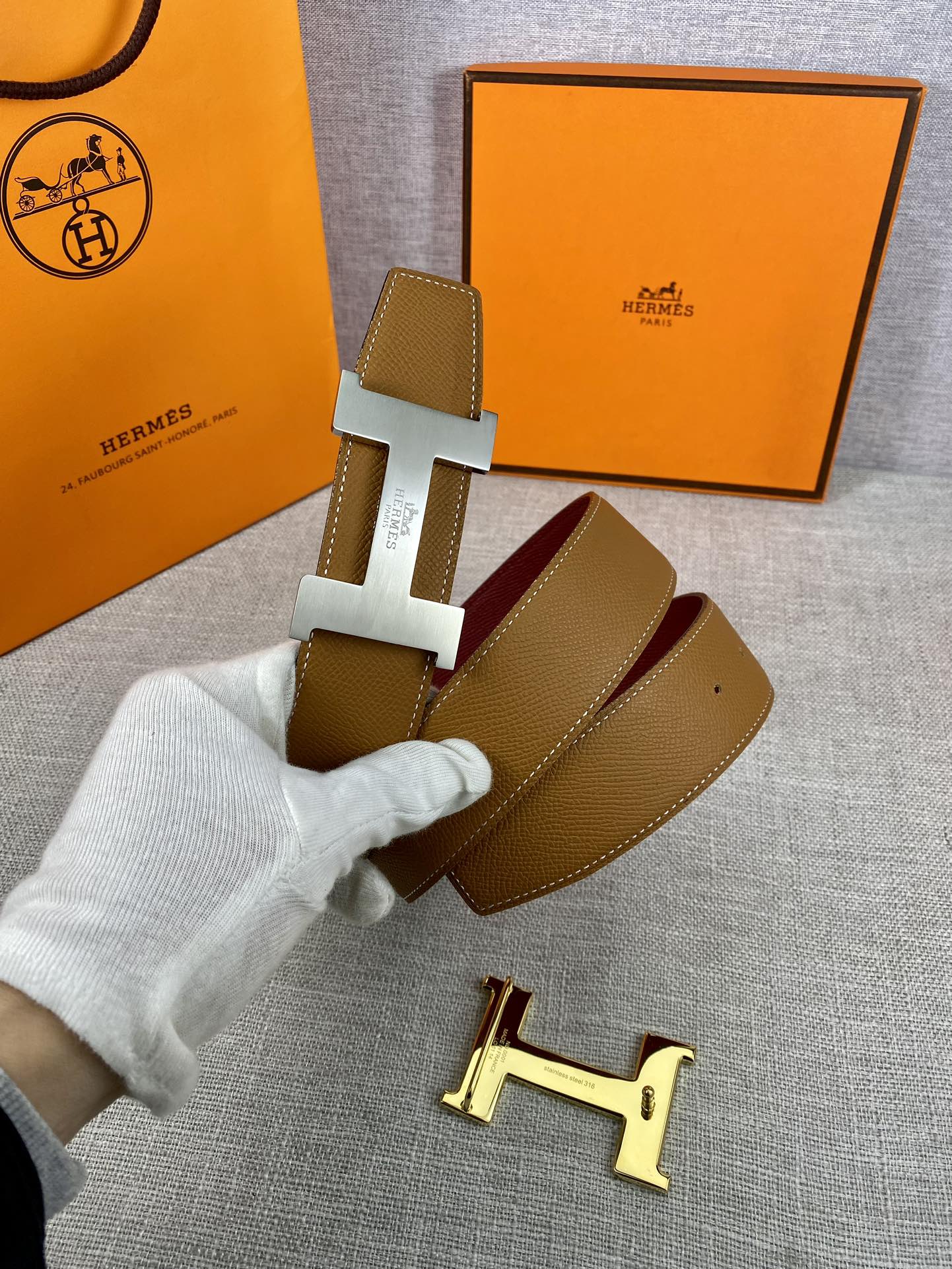 Leather belt with tan strap and gold H buckle, burgundy keeper card visible.
