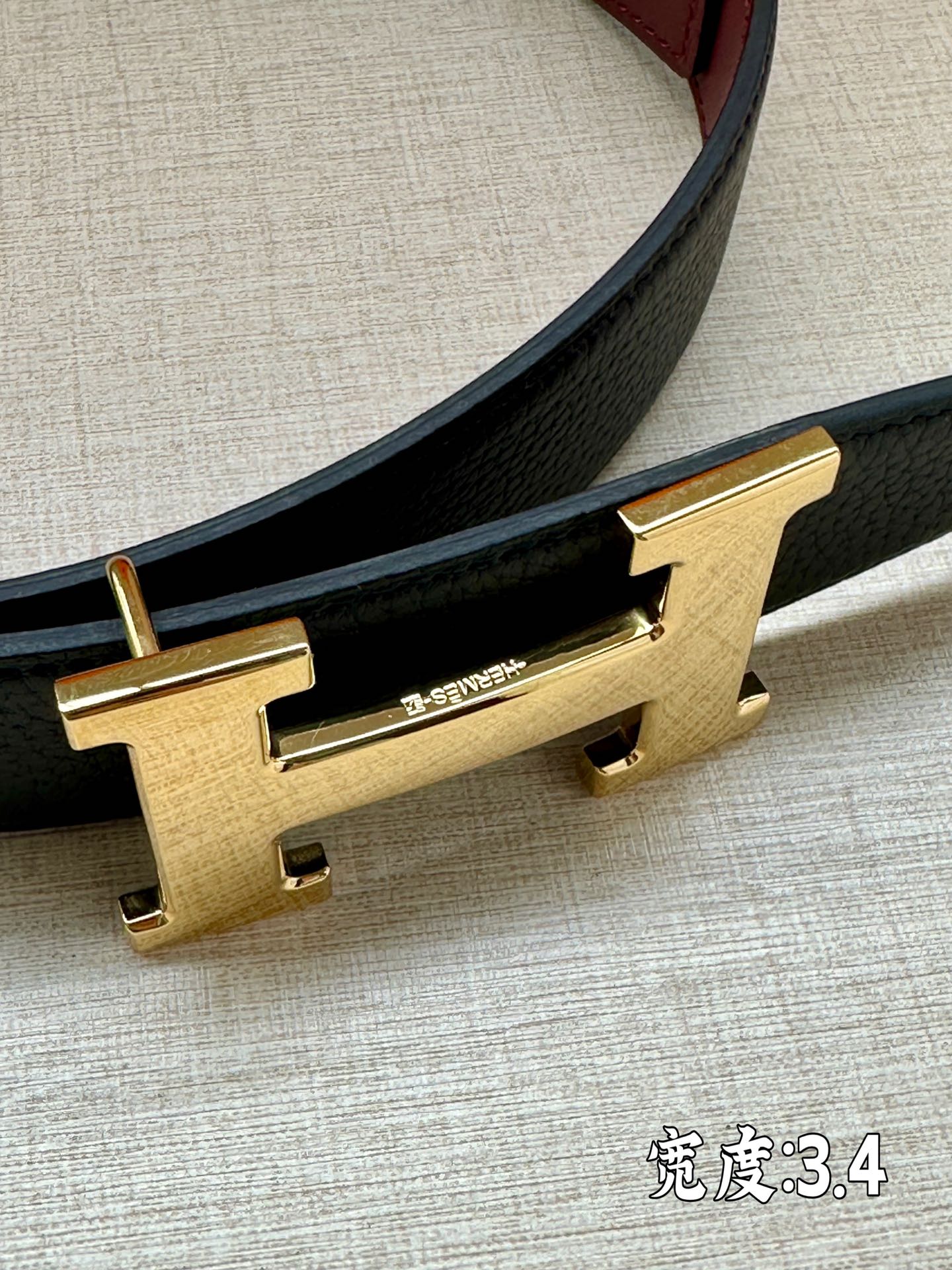 Leather belt buckle close-up with gold-tone H and engraved lettering