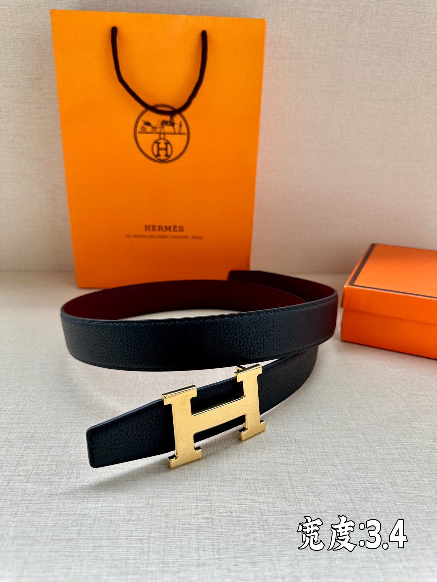 Leather belt with dark strap and gold-tone H buckle, laid flat