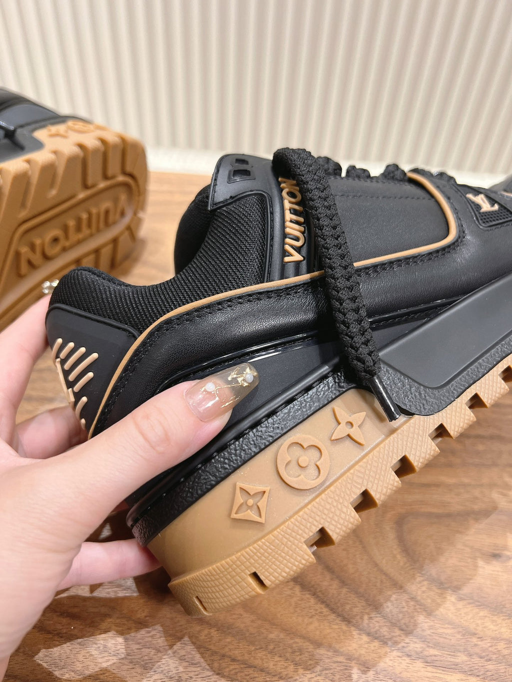 Black trainer sneaker side close-up with tan rubber sole and LV monogram accents