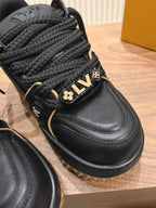 Black trainer sneaker close-up with braided laces and LV plaque, gold trim