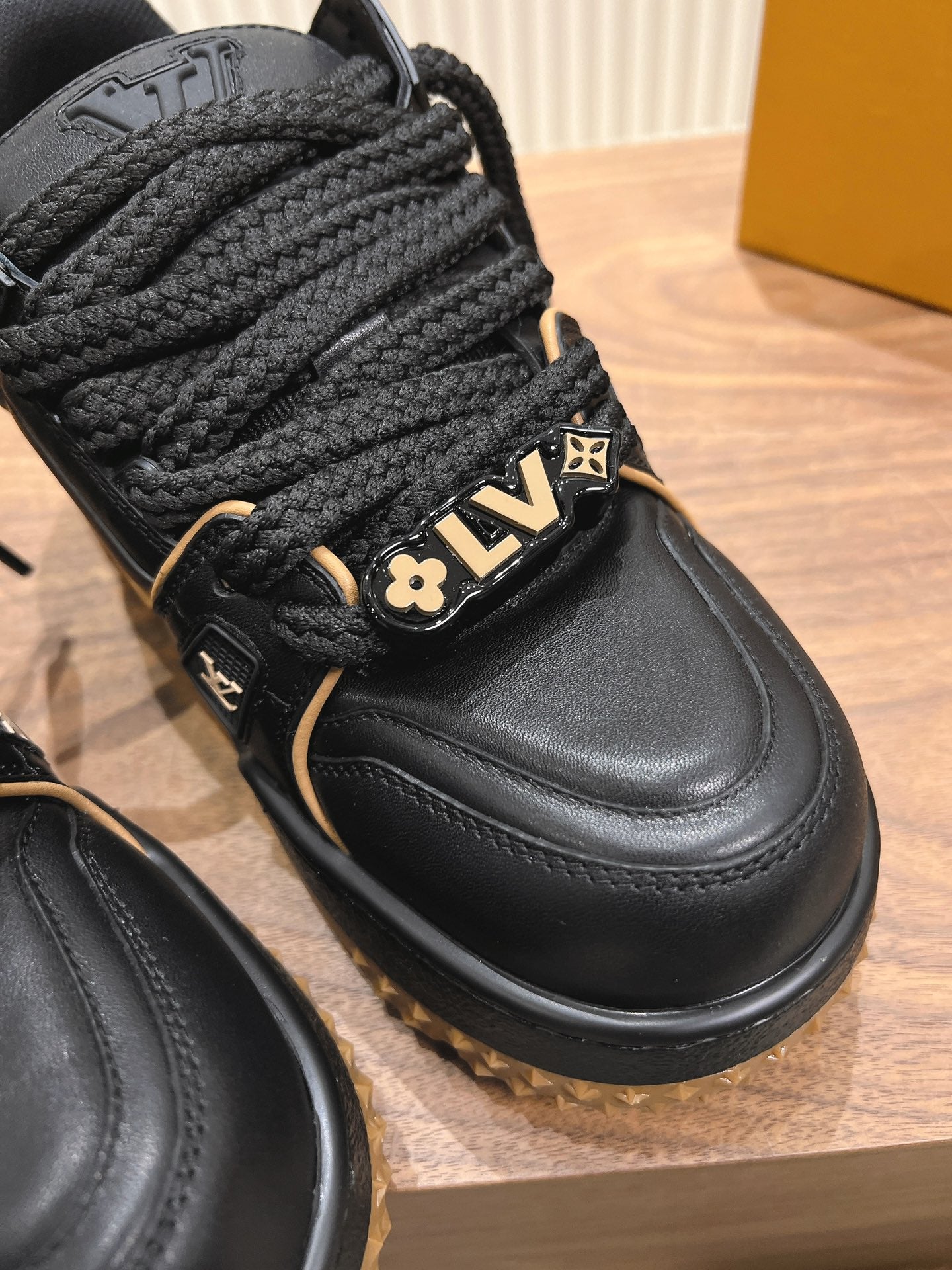 Black trainer sneaker close-up with braided laces and LV plaque, gold trim