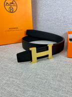 Black leather belt with gold-toned H buckle on a gray fabric surface