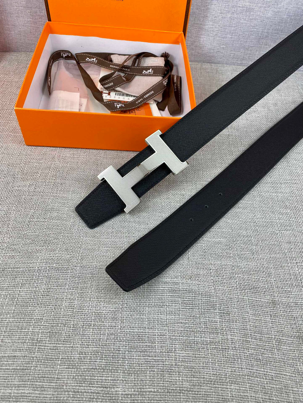 Black leather belt with silver-toned H buckle laid flat
