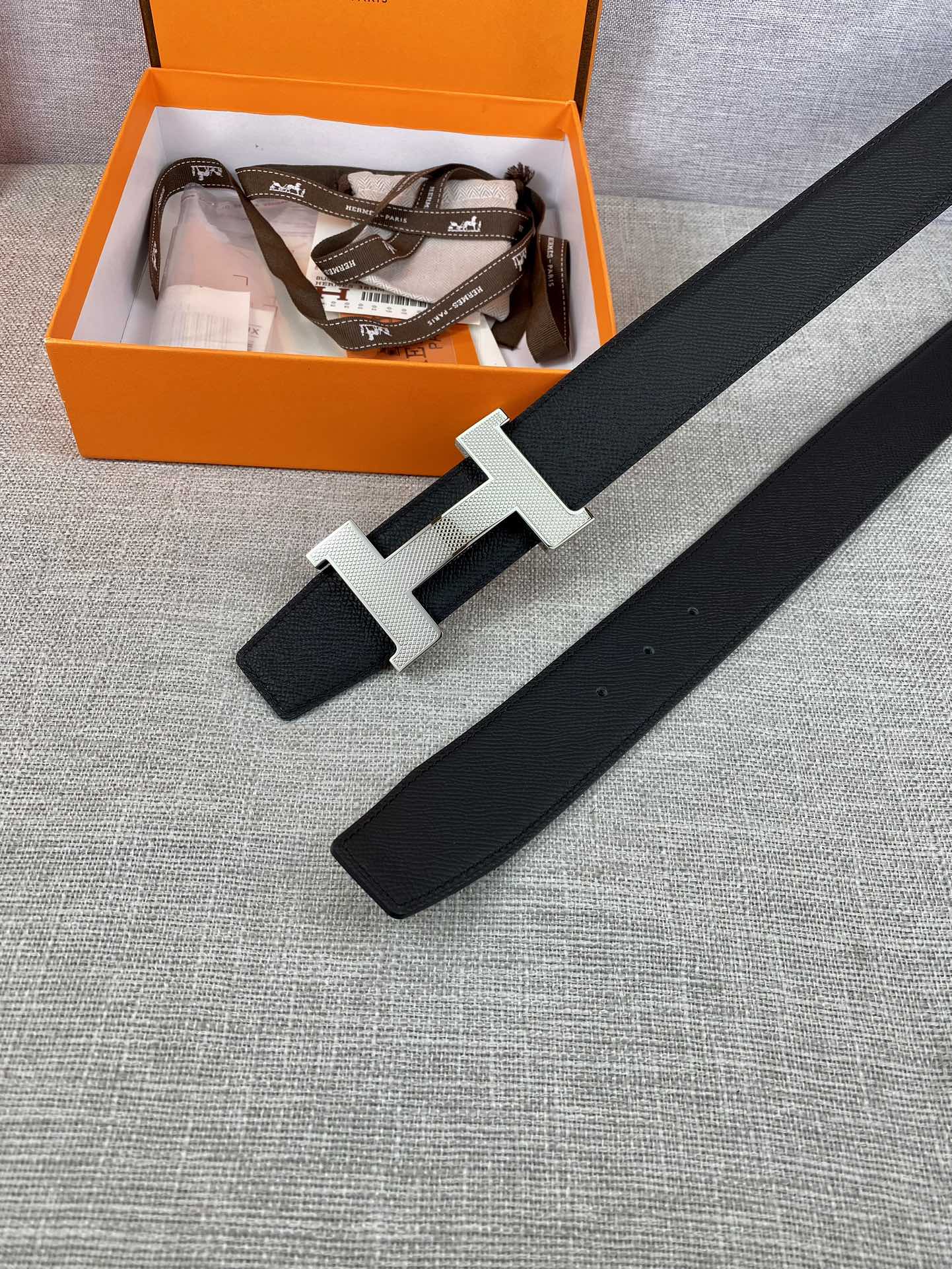 Black leather belt with silver-toned H buckle laid flat
