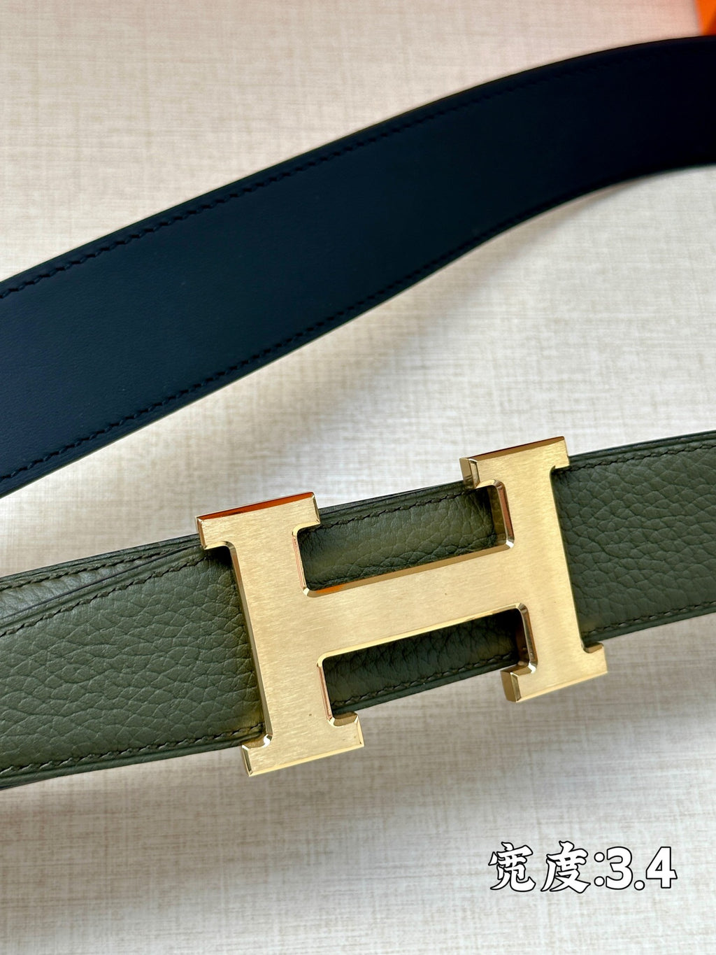 Green leather belt strap with gold-tone H buckle, close-up