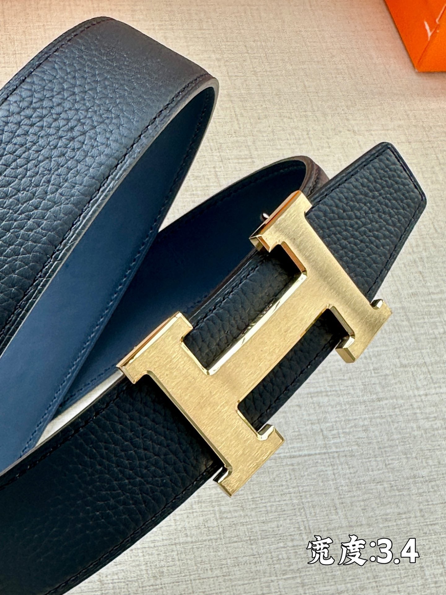 Hermes belt close-up of dark blue leather strap with gold H buckle