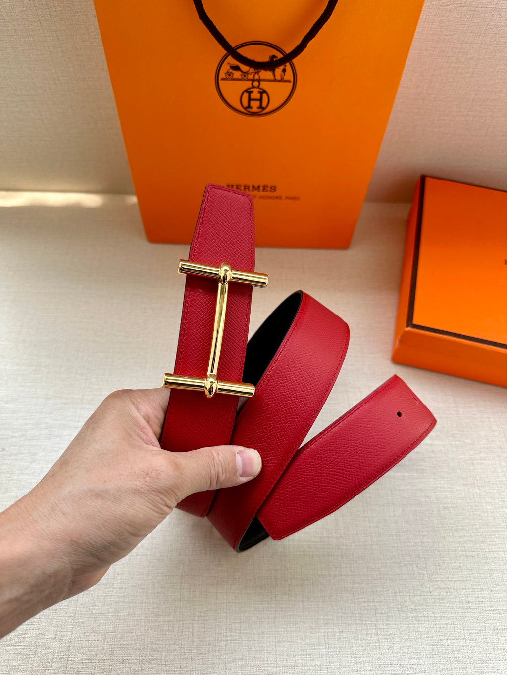 Red leather belt strap with rectangular gold-tone buckle hardware, side view.