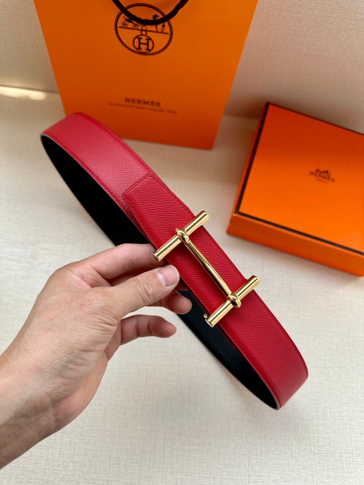 Red leather belt with gold-tone double-prong buckle and textured finish.