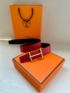 Reversible leather belt: red strap with gold-tone buckle and black underside detail.