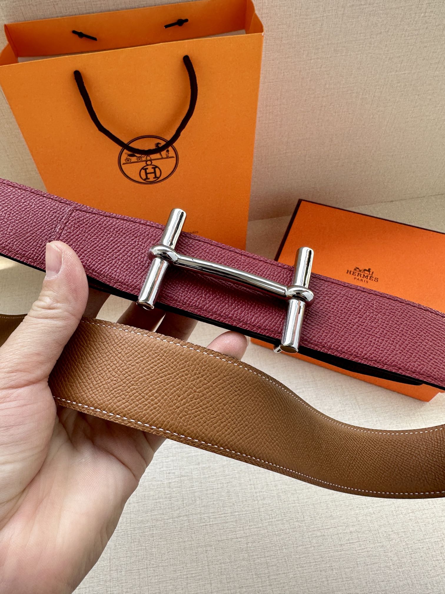 Reversible leather belt showing burgundy and tan sides with silver double-prong buckle