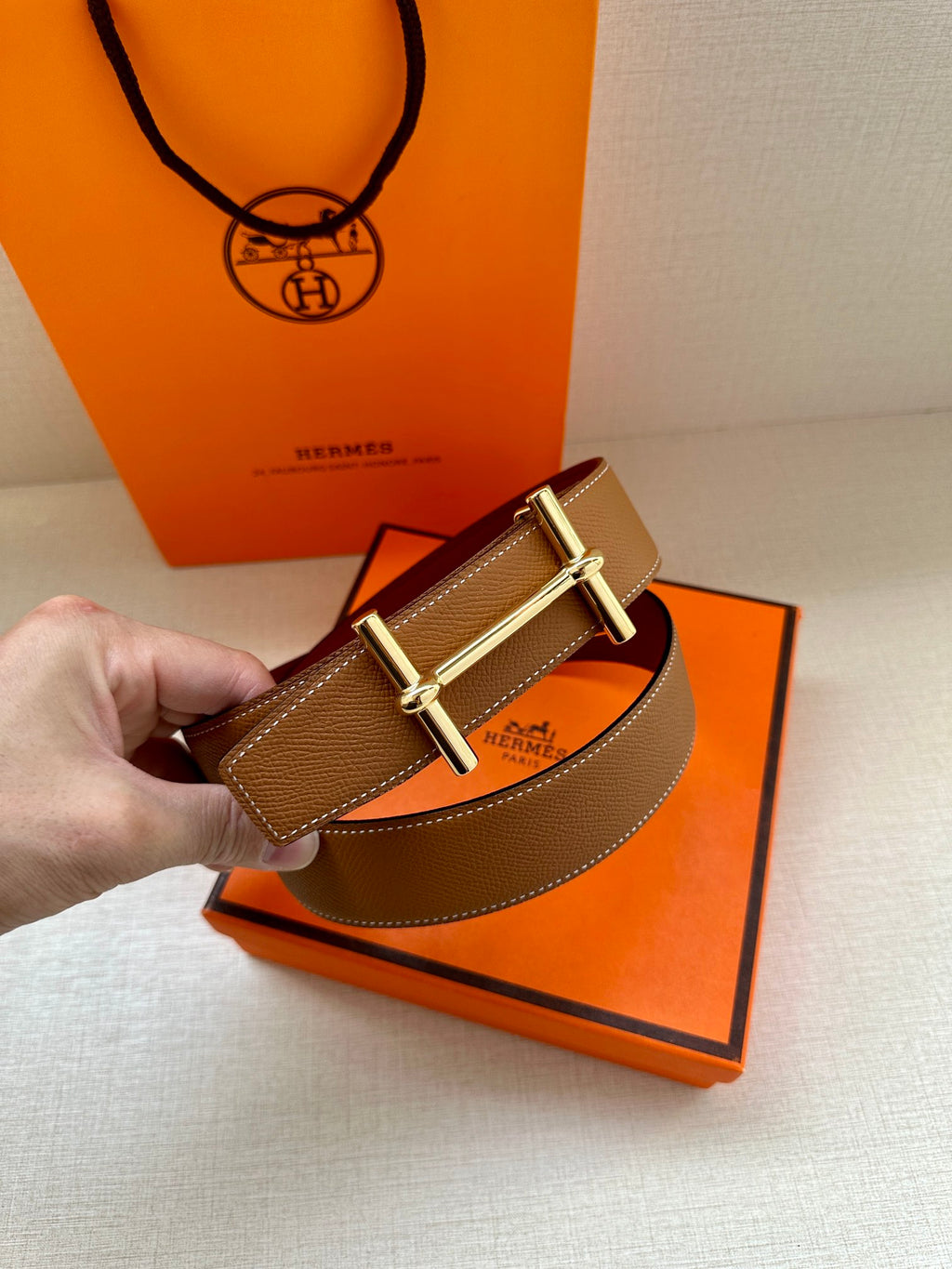 Hermes belt with tan strap and silver H buckle, shown over a box