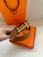 Tan leather belt with gold double-prong buckle held near retail boxes