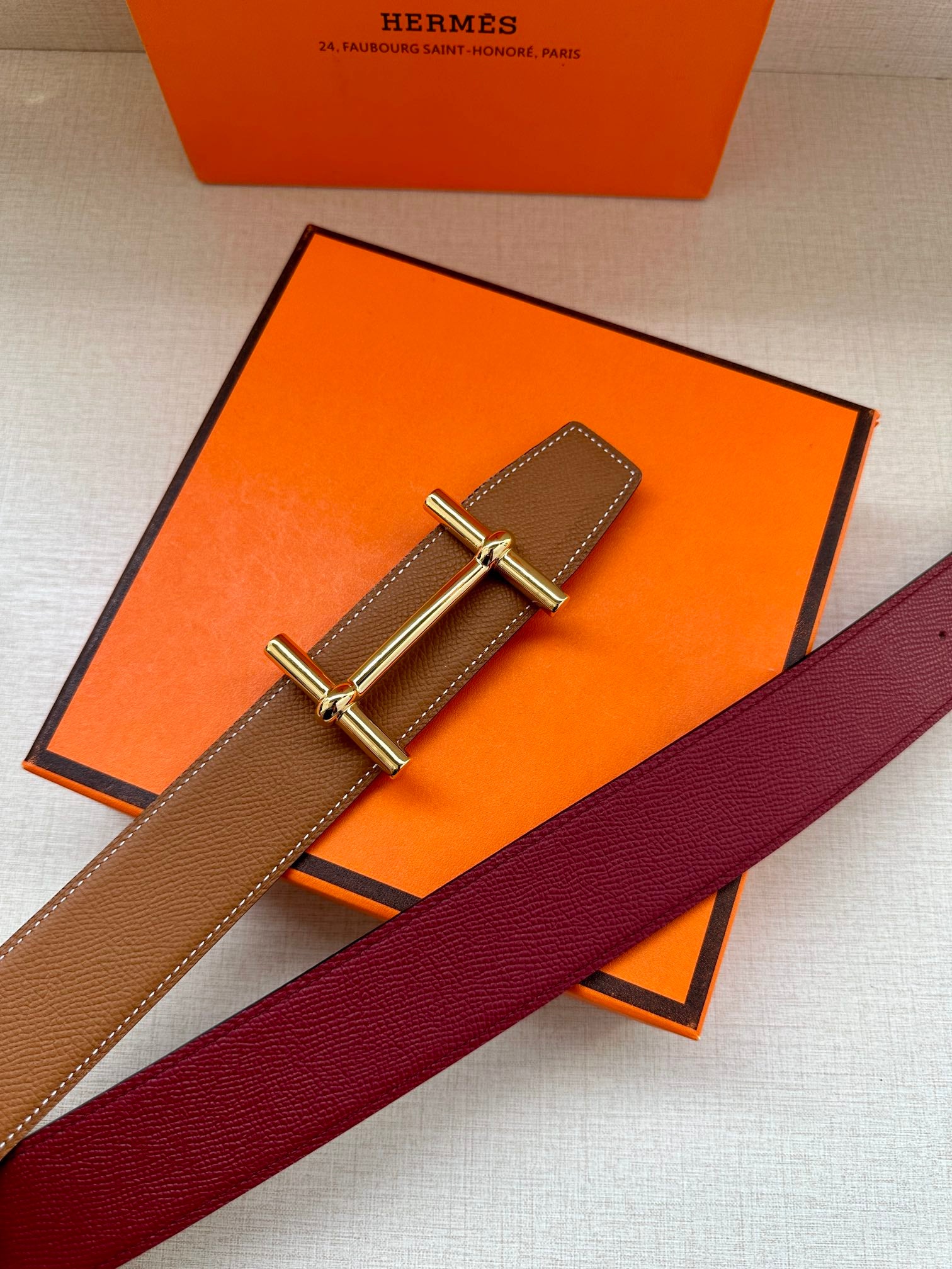 Hermes belt detail: tan strap with silver H buckle on orange box