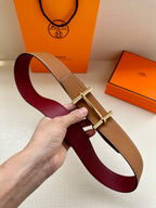 Hermes belt with burgundy and tan straps and silver H buckle, held in hand