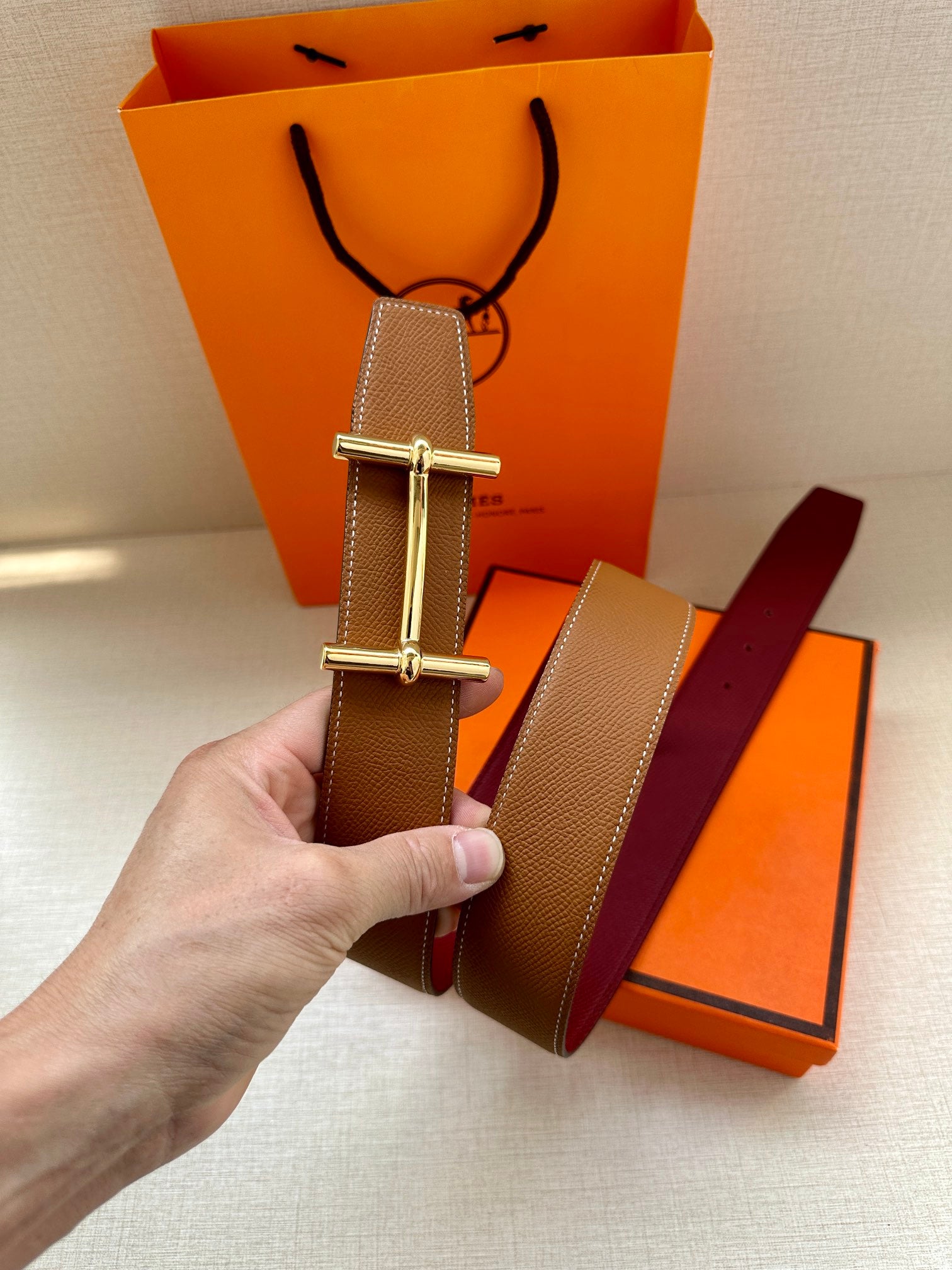 Hermes belt with brown strap and silver H buckle, next to tan strap