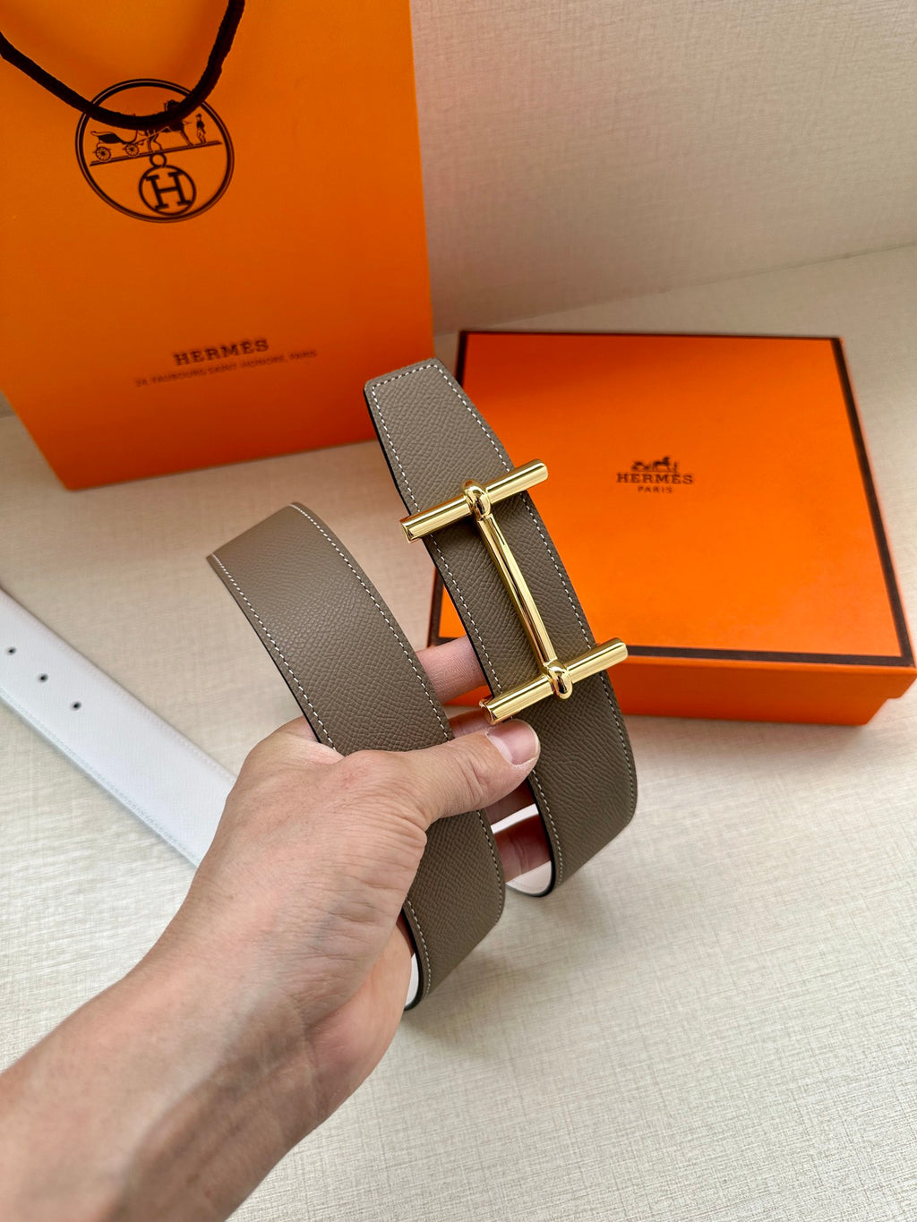 Taupe leather belt with gold double-prong buckle and white underside visible
