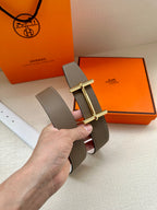 Taupe leather belt with gold double-prong buckle and white underside visible