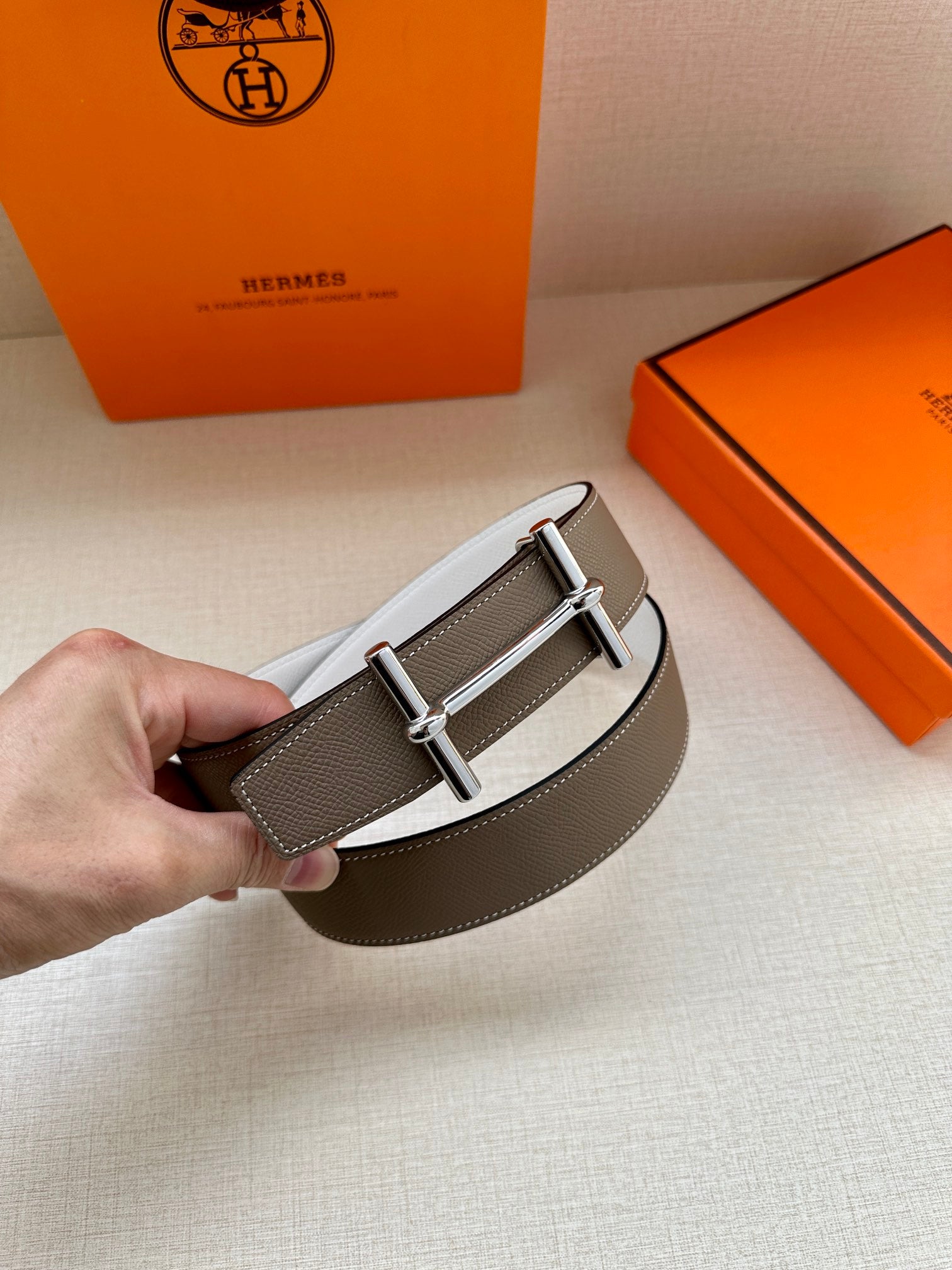 Taupe leather belt with silver double-prong buckle and white reverse strap