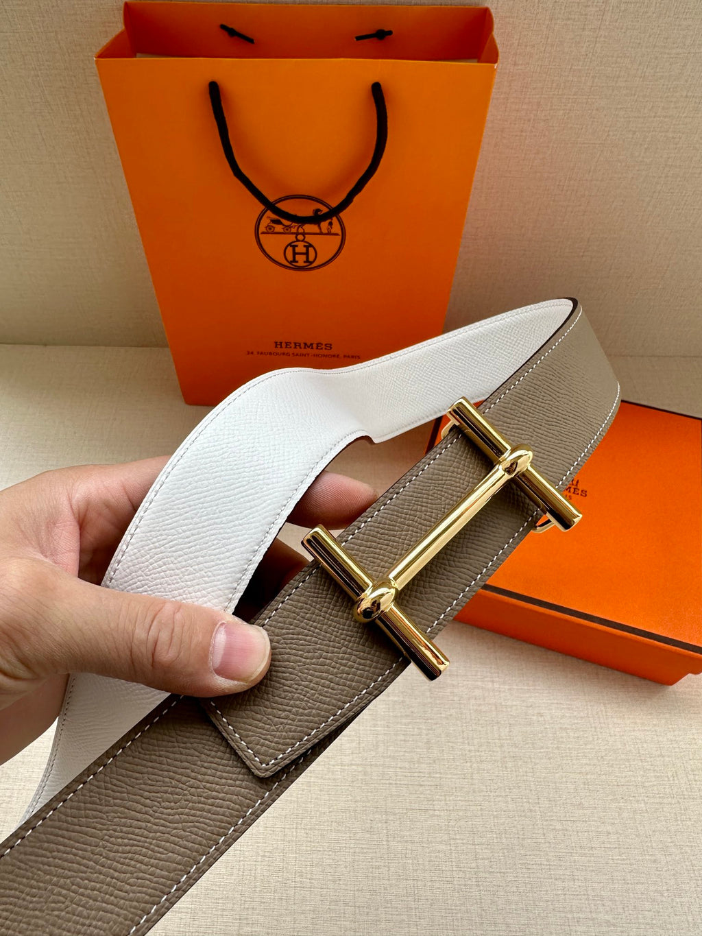 Taupe leather belt with gold double-prong buckle, close-up of strap end