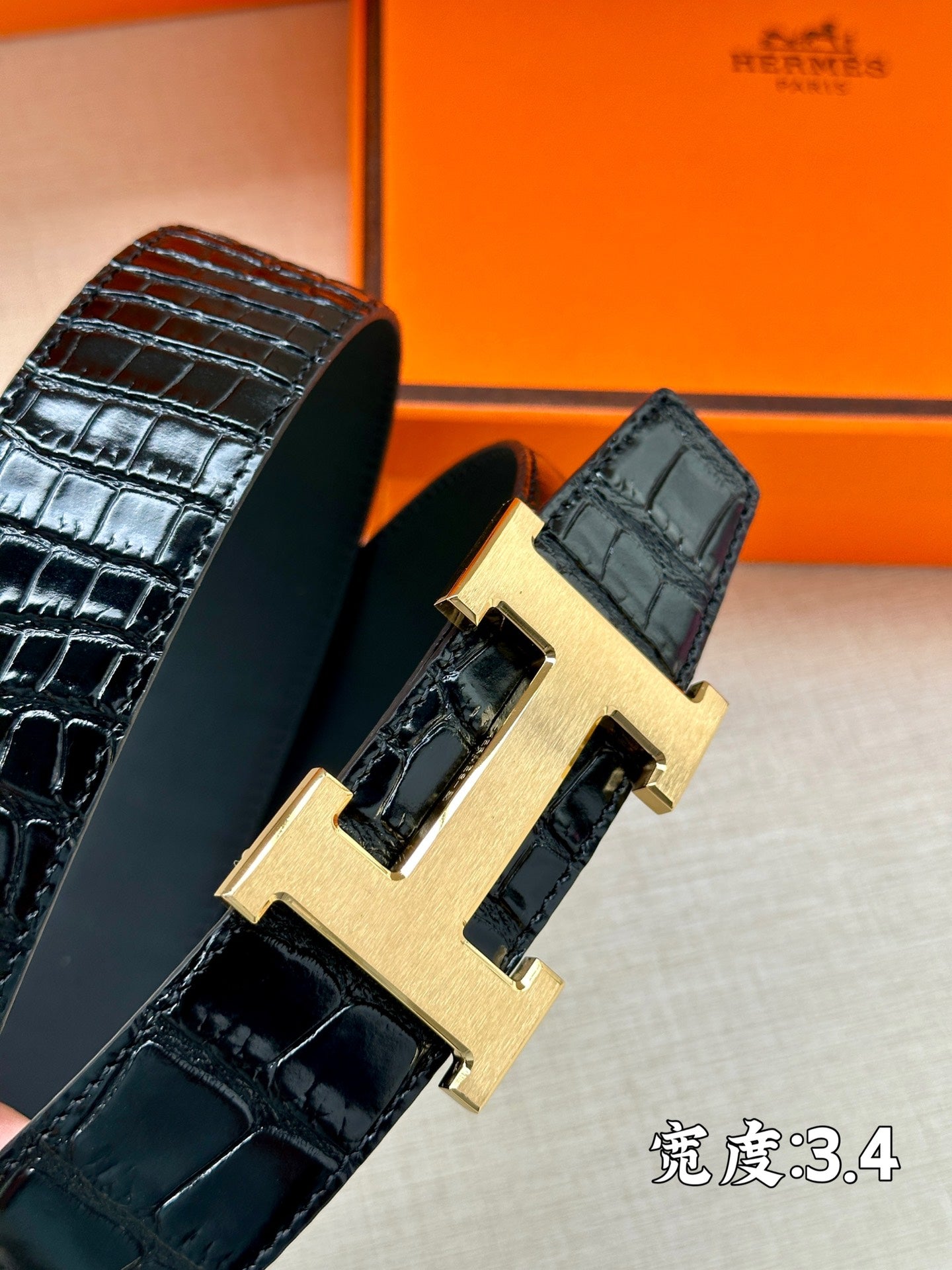 Hermes belt close-up: dark embossed leather with gold-toned H buckle hardware.