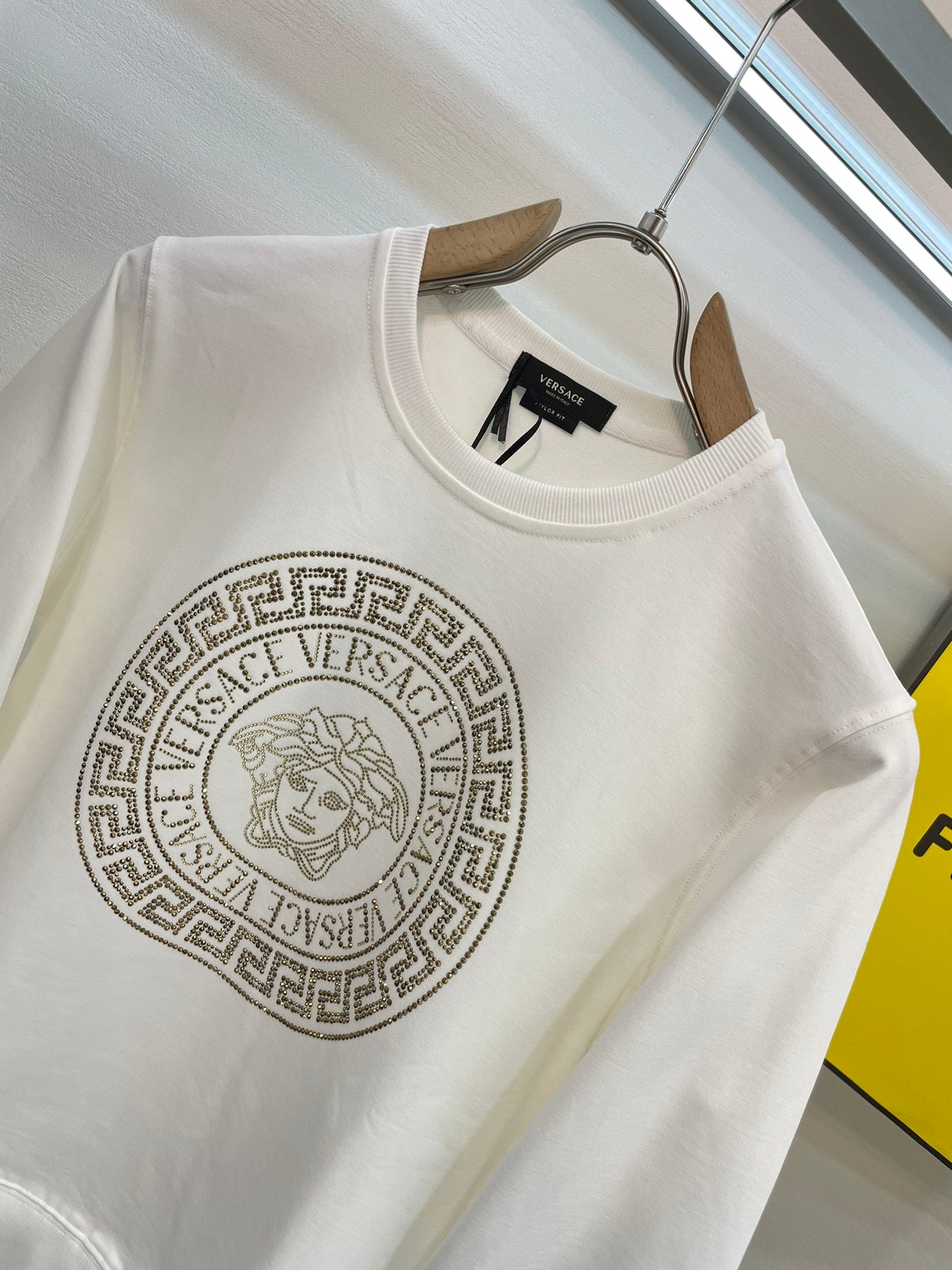 White crewneck sweatshirt with gold medallion logo detail at chest