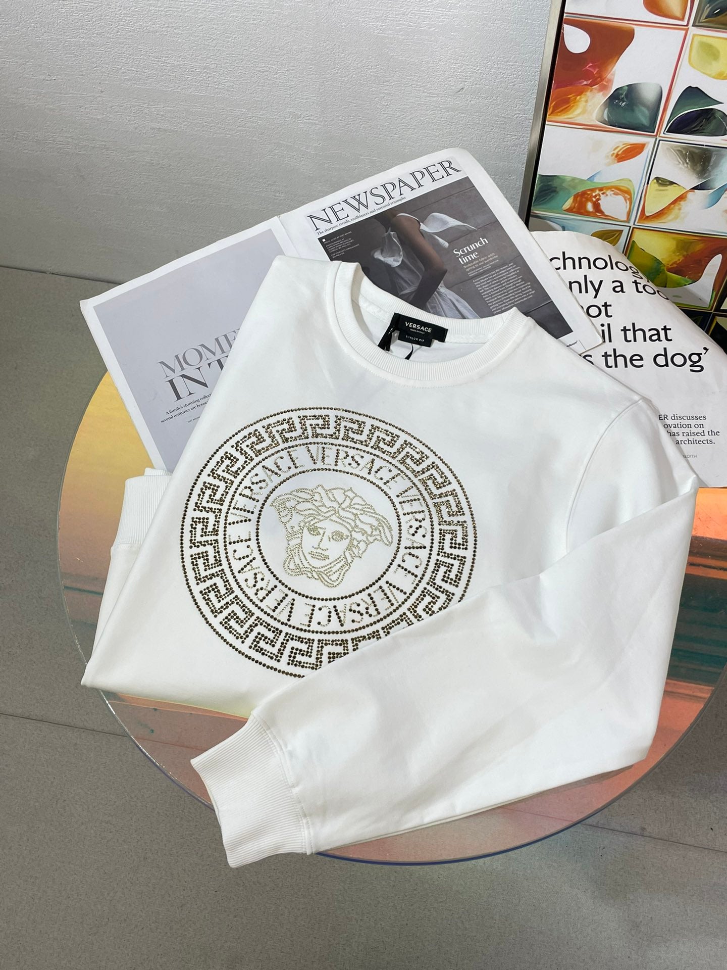 White crewneck sweatshirt folded with front gold medallion logo print