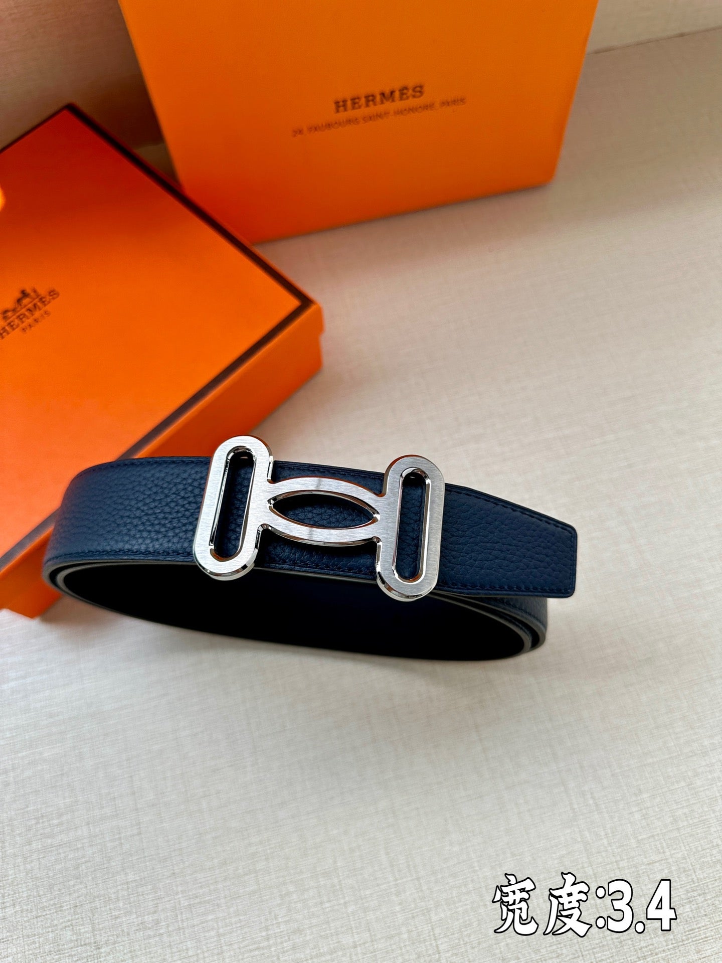 Hermes belt, dark blue leather strap with silver-tone buckle detail, angled.