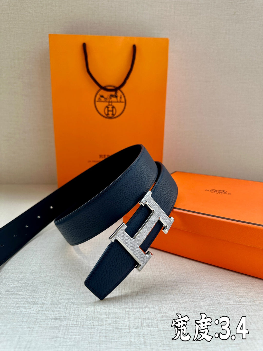Dark blue leather belt with silver Hermès H buckle, angled view showing strap width