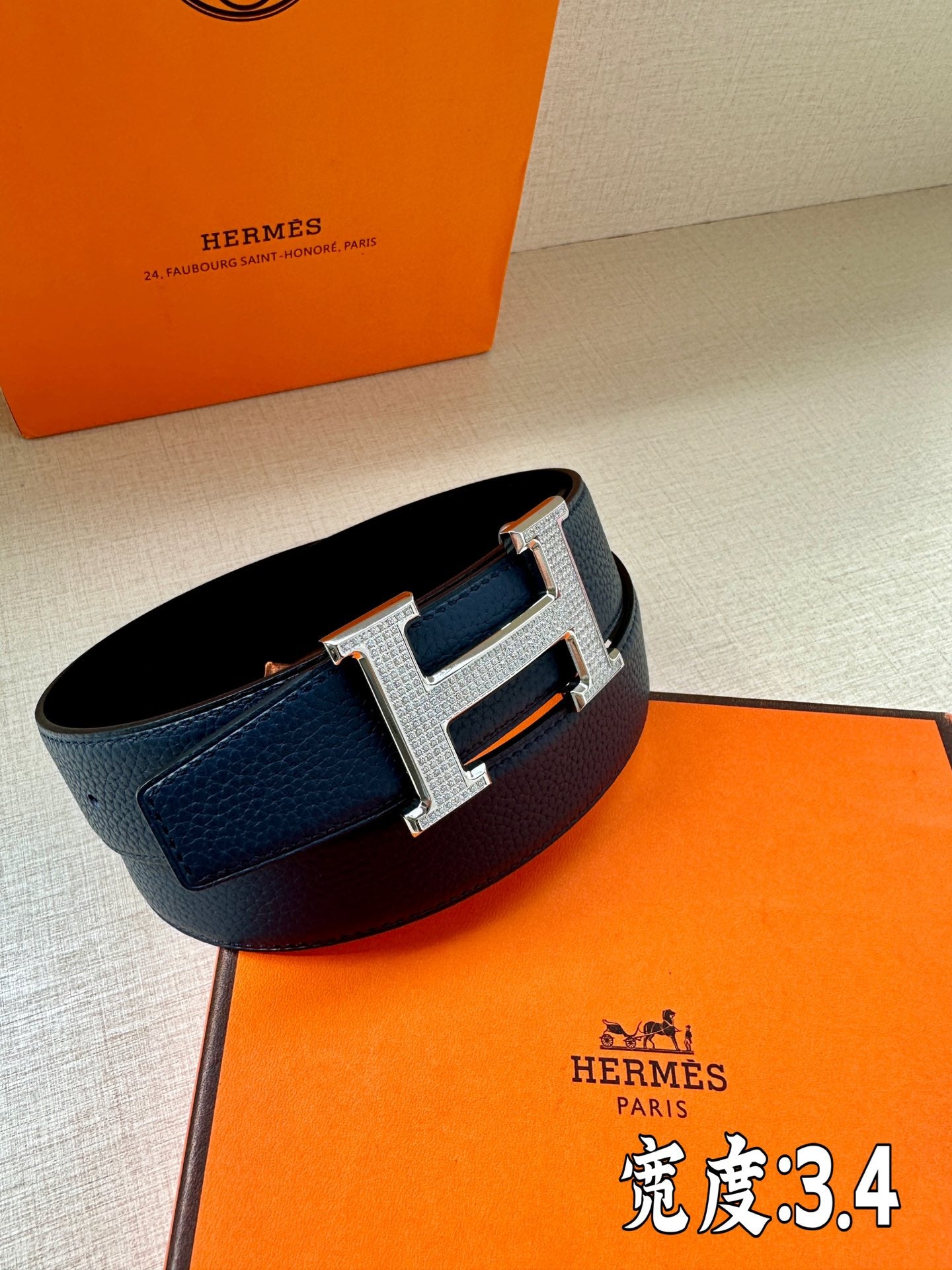 Dark blue leather belt with silver Hermès H buckle, side view of strap edge
